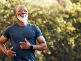 Happy black man running in park with music, smile and mockup in nature, garden and workout. Senior male, outdoor runner and motivation for fitness, energy and healthy exercise training with earphones