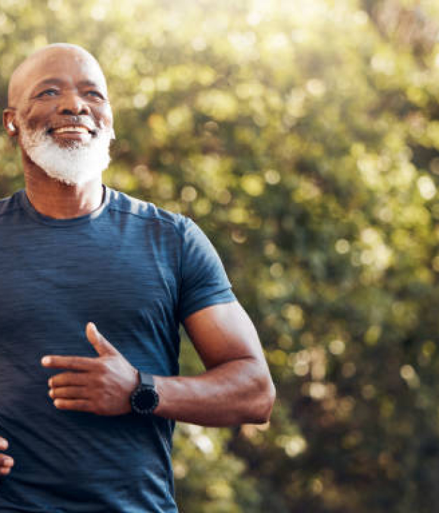 Happy black man running in park with music, smile and mockup in nature, garden and workout. Senior male, outdoor runner and motivation for fitness, energy and healthy exercise training with earphones